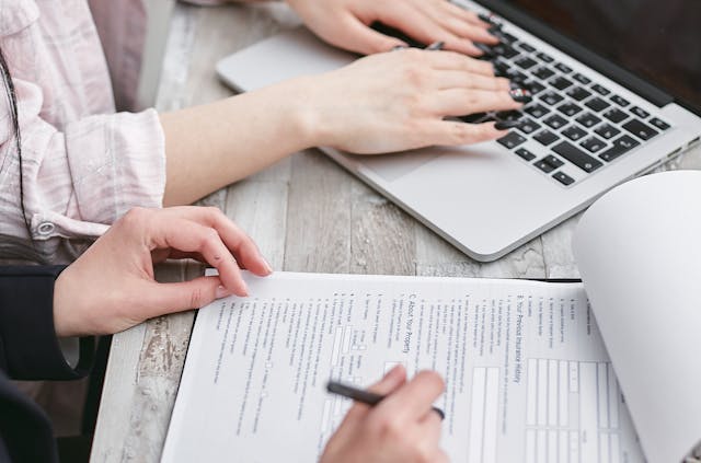 person typing on computer and writing on paper